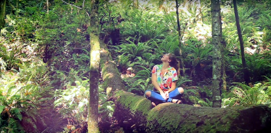 Photo showing a women sitting on a tree trunk in dense forest.