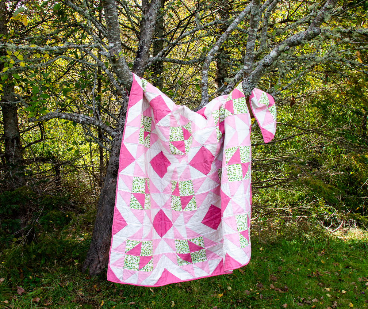 photo of a pik and green quilt hanging in a tree